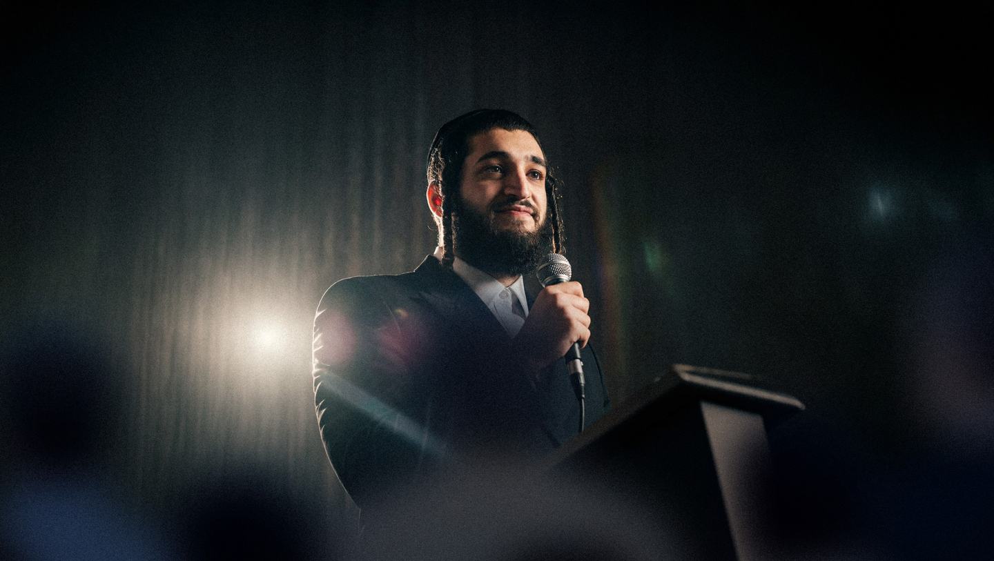 Mayer speaking on stage with a microphone